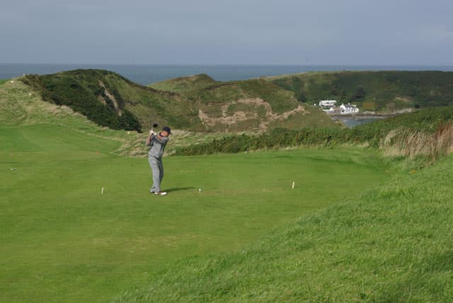 Golfer teeing off at Nefyn & District Golf Club, Llŷn Peninsula, Wales